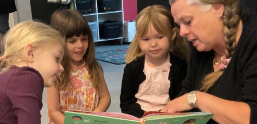 En pædagog sidder og læser bog med tre børnehavebørn