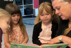 En pædagog sidder og læser bog med tre børnehavebørn